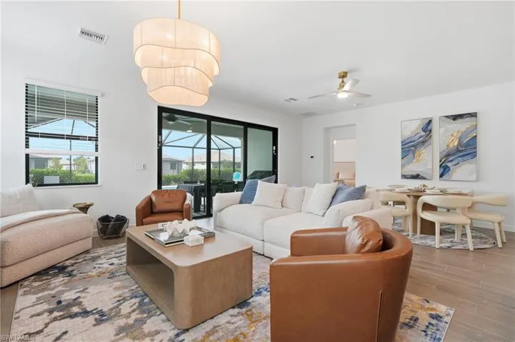 Open-concept living space featuring wood-finish flooring, a contemporary tiered chandelier, and direct access to the screened patio through sliding glass doors