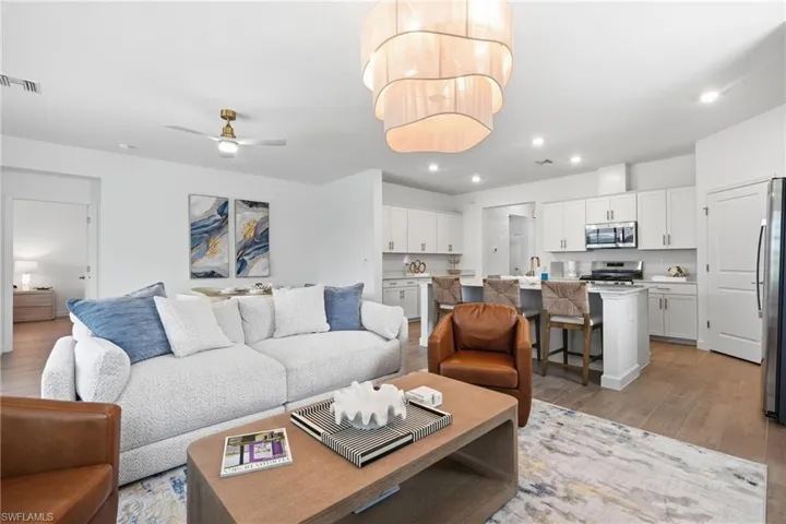 Open-concept living space featuring wood-finish flooring, a contemporary chandelier, recessed lighting, and a kitchen with white cabinetry and stainless steel appliances