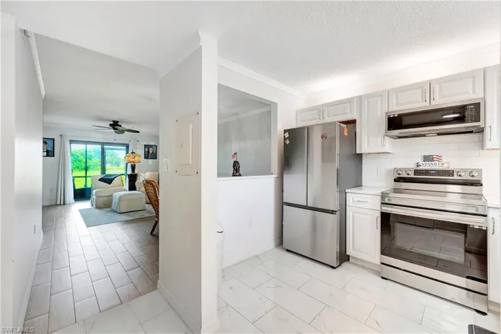 Kitchen with light tile patterned floors, white cabinets, backsplash, ceiling fan, and stainless steel appliances