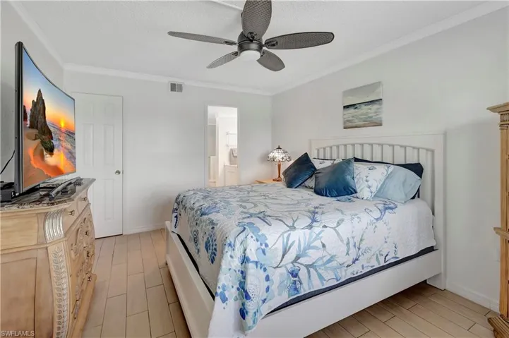 Bedroom with crown molding, light wood-type flooring, ceiling fan, and connected bathroom