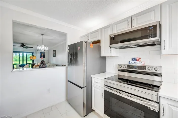 Kitchen featuring light tile patterned flooring, backsplash, ceiling fan with notable chandelier, appliances with stainless steel finishes, and pendant lighting