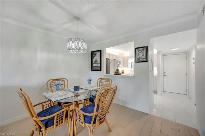 Dining area with crown molding, a textured ceiling, a notable chandelier, and light tile patterned floors