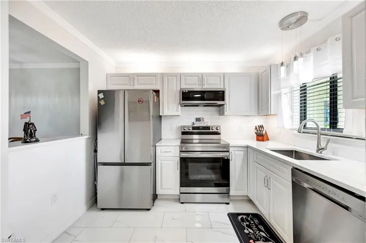 Kitchen featuring light tile patterned flooring, sink, appliances with stainless steel finishes, and ornamental molding