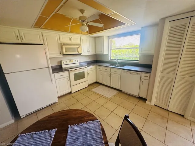 Kitchen with white appliances, a sink, dark countertops, light tile patterned floors, and a ceiling fan