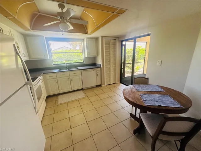 Kitchen with white appliances, a sink, dark countertops, light tile patterned floors, and a tray ceiling