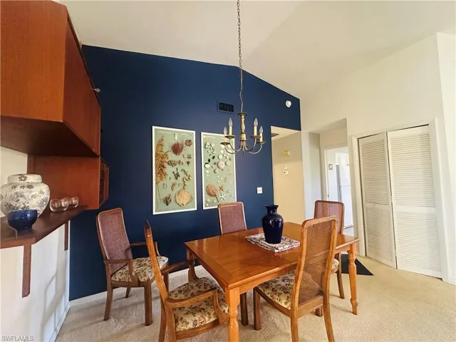 Dining space with light colored carpet, a chandelier, and high vaulted ceiling