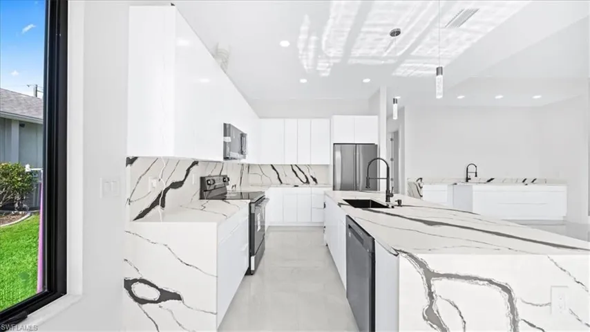 Kitchen with light stone counters, modern cabinets, stainless steel appliances, white cabinetry, and a center island with sink