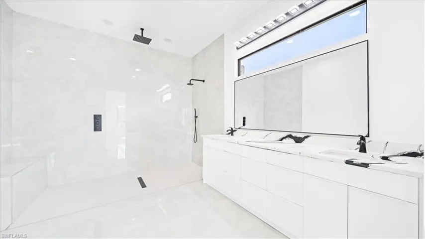 Bathroom with double vanity, a marble finish shower, and light marble finish flooring