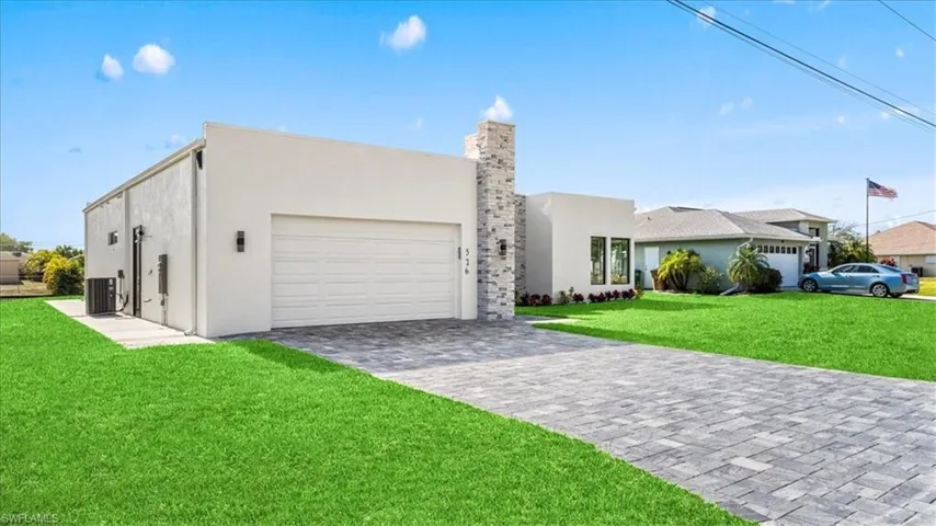 Modern home featuring a front lawn, stucco siding, decorative driveway, a garage, and a chimney