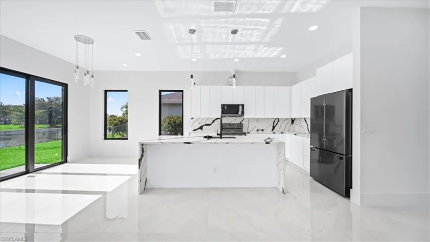 Kitchen with hanging light fixtures, freestanding refrigerator, white cabinetry, light stone counters, and recessed lighting