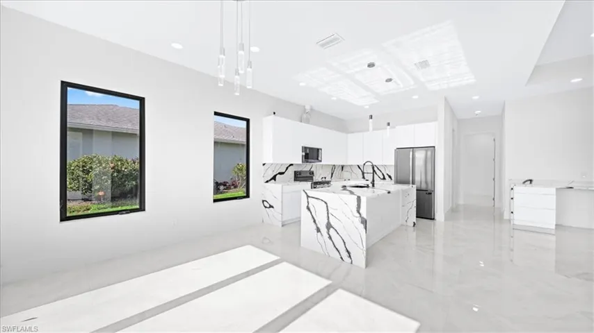 Kitchen with appliances with stainless steel finishes, white cabinetry, a center island with sink, pendant lighting, and light marble finish floors
