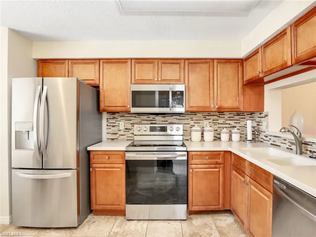 Kitchen with appliances with stainless steel finishes, brown cabinetry, tasteful backsplash, light tile patterned floors, and a textured ceiling