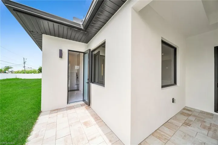 View of exterior entry with a patio area and a lawn