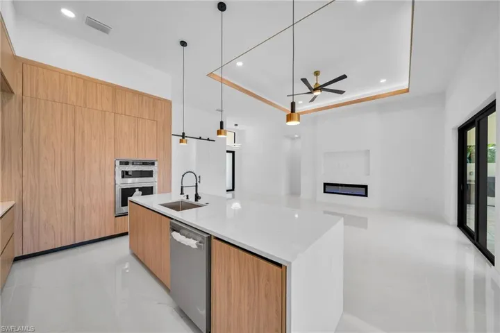 Kitchen with ceiling fan, an island with sink, stainless steel appliances, a tray ceiling, and light stone countertops