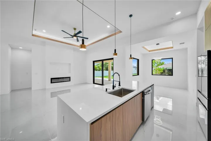 Kitchen featuring a tray ceiling, a center island with sink, sink, light tile patterned floors, and ceiling fan