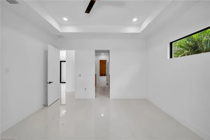 Tiled empty room with ceiling fan and a tray ceiling