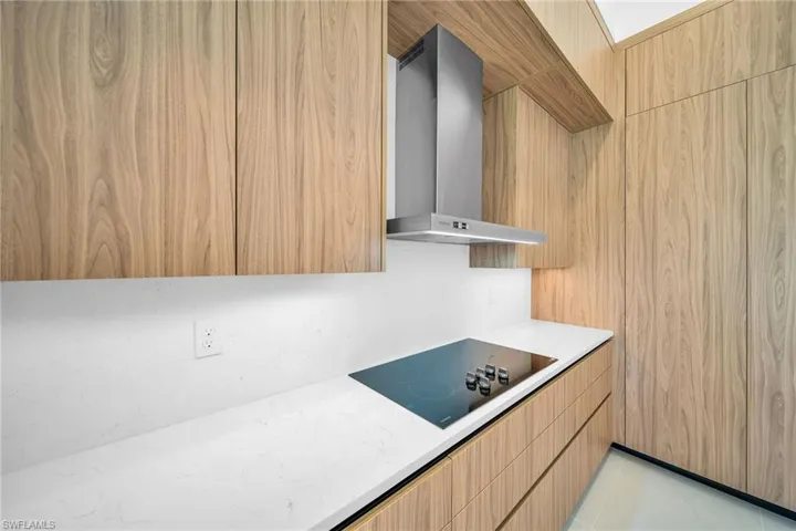 Kitchen with light tile patterned flooring, black electric cooktop, and wall chimney exhaust hood
