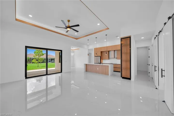 Unfurnished living room featuring light tile patterned flooring, a barn door, ceiling fan, and a tray ceiling