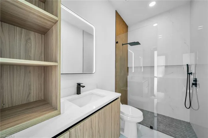 Bathroom with tiled shower, tile patterned floors, toilet, and vanity