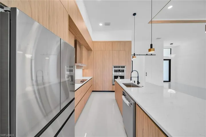 Kitchen featuring stainless steel appliances, hanging light fixtures, wall chimney exhaust hood, sink, and light stone countertops