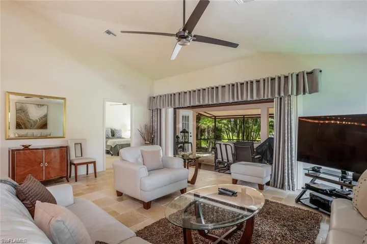 Living room featuring a ceiling fan, high vaulted ceiling, and light stone finish flooring