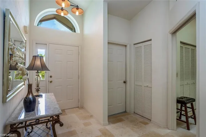 Entrance foyer with light stone finish floors, a chandelier, and a towering ceiling