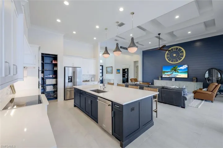Kitchen featuring coffered ceiling, hanging light fixtures, a center island with sink, white cabinets, and appliances with stainless steel finishes