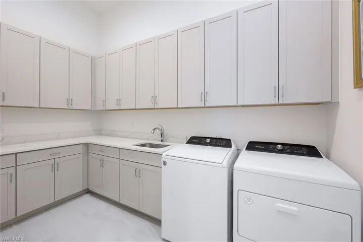 Clothes washing area featuring separate washer and dryer, sink, light tile flooring, and cabinets