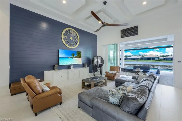 Living room featuring coffered ceiling, light tile flooring, ceiling fan, and wood walls