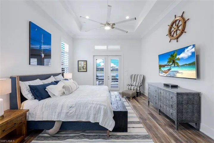Bedroom with ceiling fan, a tray ceiling, french doors, dark wood-type flooring, and access to outside