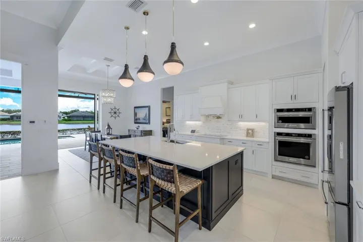 Kitchen featuring stainless steel appliances, pendant lighting, backsplash, light tile floors, and a kitchen island with sink