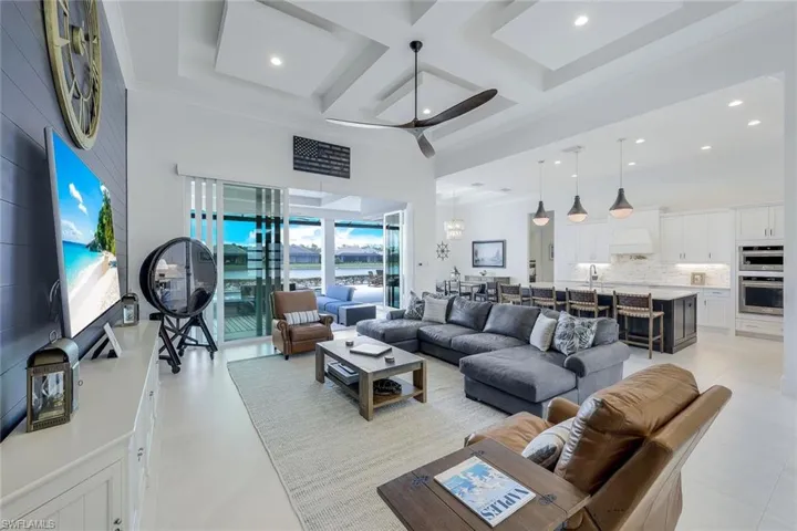 Living room featuring ceiling fan, coffered ceiling, light tile flooring, and ornamental molding