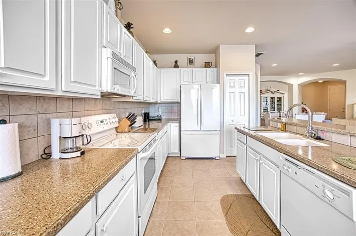 Kitchen featuring white cabinetry, sink, decorative backsplash, light tile patterned floors, and white appliances