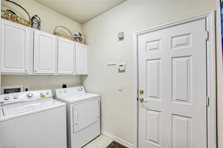 Washroom featuring cabinets, light tile patterned floors, and washing machine and clothes dryer