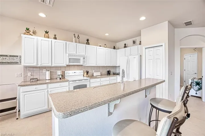 Kitchen featuring white cabinetry, light tile patterned floors, white appliances, and an island with sink