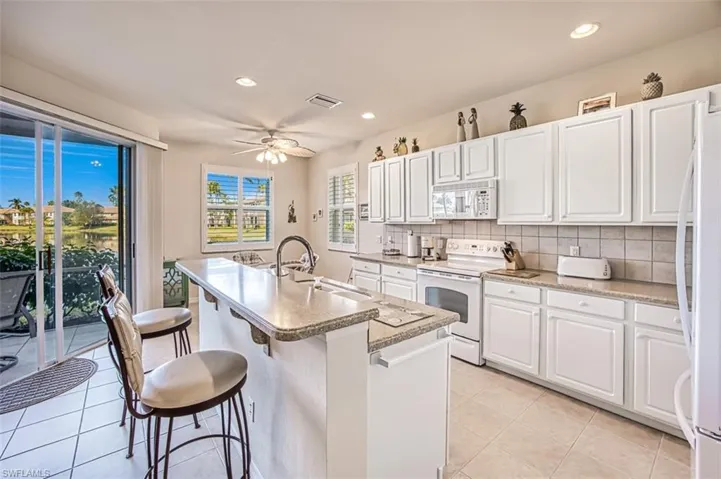 Kitchen with an island with sink, sink, white cabinets, and white appliances