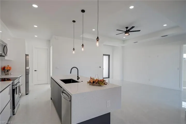 Kitchen with hanging light fixtures, white cabinetry, open floor plan, appliances with stainless steel finishes, and a raised ceiling