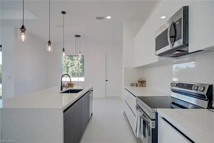 Kitchen featuring stainless steel appliances, white cabinets, hanging light fixtures, light stone counters, and recessed lighting