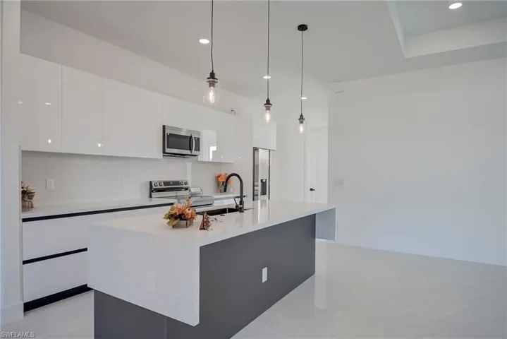 Kitchen featuring decorative light fixtures, appliances with stainless steel finishes, white cabinetry, modern cabinets, and an island with sink