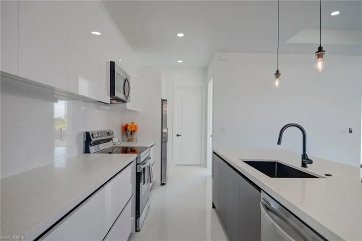 Kitchen with modern cabinets, stainless steel appliances, white cabinetry, pendant lighting, and light stone counters
