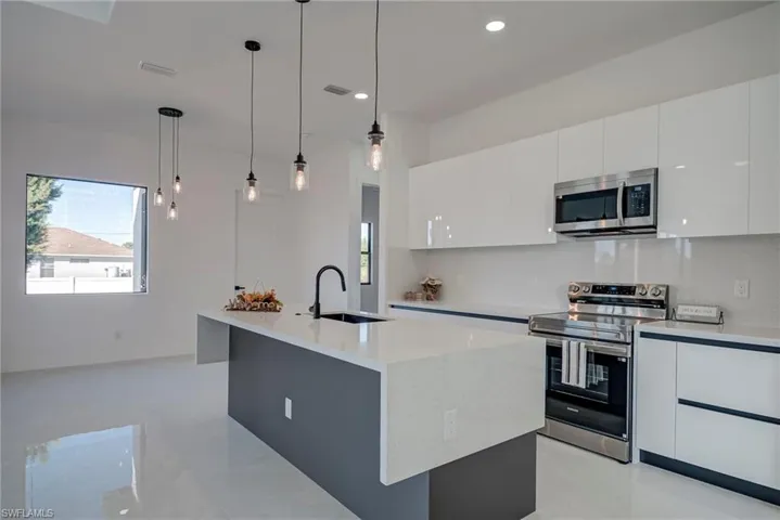 Kitchen with stainless steel appliances, modern cabinets, decorative light fixtures, a kitchen island with sink, and white cabinets