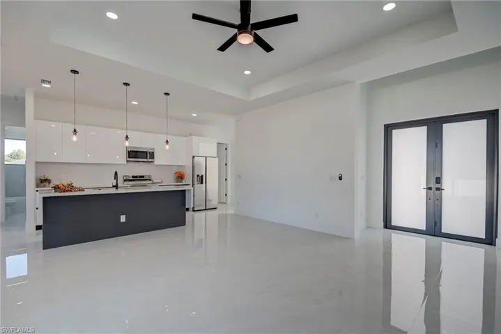 Kitchen featuring open floor plan, white cabinets, a raised ceiling, an island with sink, and a high ceiling