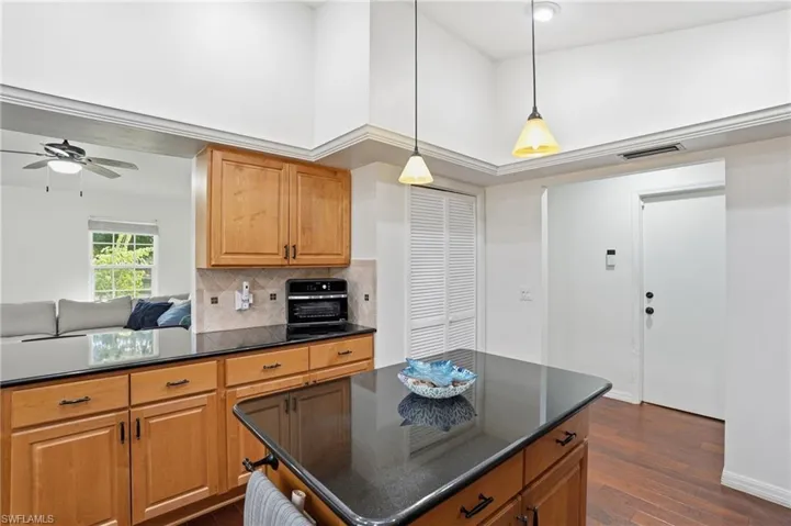 Kitchen with a towering ceiling, decorative backsplash, a center island, dark stone counters, and dark wood finished floors