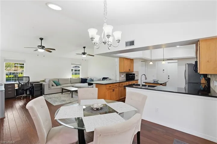 Dining room with ceiling fan, dark wood finished floors, a chandelier, a desk, and lofted ceiling