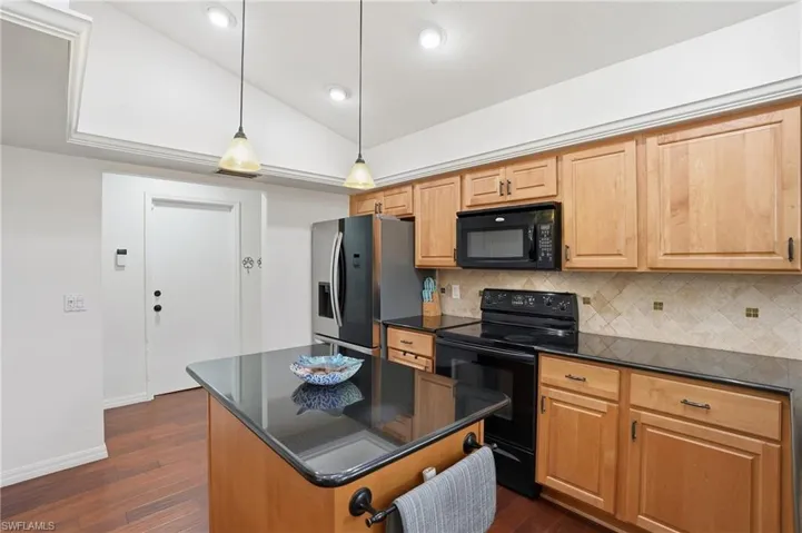 Kitchen featuring black appliances, lofted ceiling, a center island, hanging light fixtures, and dark wood-style flooring