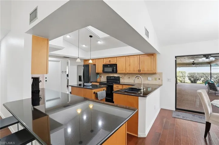 Kitchen with a center island, a peninsula, black appliances, decorative light fixtures, and decorative backsplash