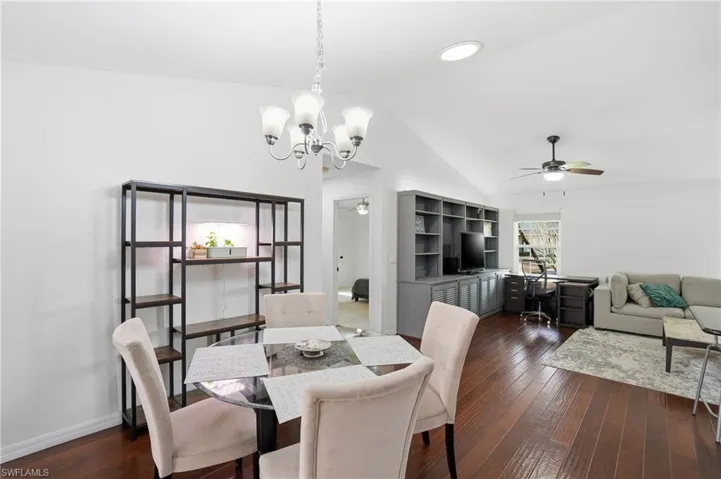 Dining area featuring a ceiling fan, dark wood-style floors, vaulted ceiling, a chandelier, and a desk