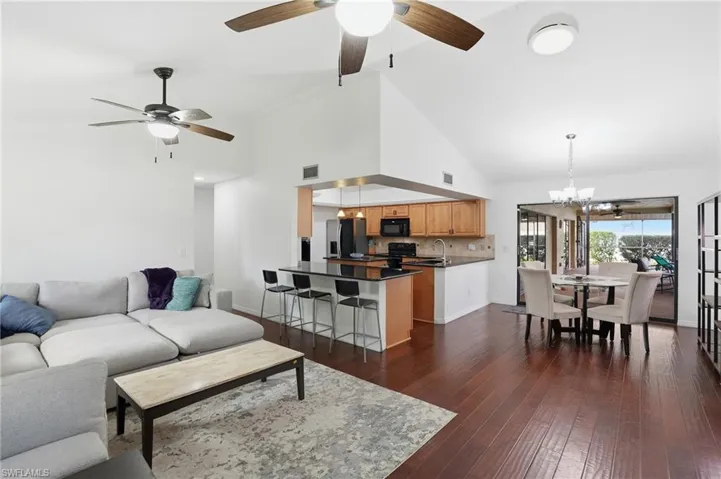 Living room with a chandelier, dark wood-type flooring, high vaulted ceiling, and ceiling fan