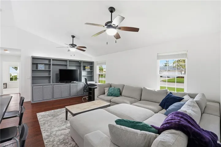 Living room featuring vaulted ceiling, dark wood-style floors, plenty of natural light, a ceiling fan, and a desk