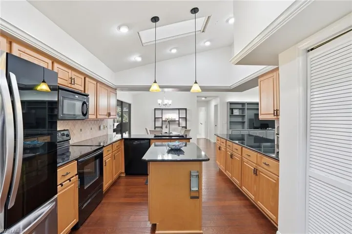 Kitchen with vaulted ceiling, a peninsula, black appliances, hanging light fixtures, and dark wood-style floors